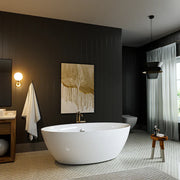 Modern bathroom with white freestanding tub, dark walls, gold-toned wall art, and soft lighting from a wall sconce and pendant lamp.