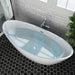 Modern white freestanding bathtub filled with water, set against gray subway tile wall and black hexagonal floor tiles, with green plant in corner.