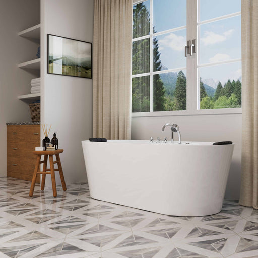 Modern white freestanding bathtub near large windows with forest view, wooden stool with toiletries, geometric tile floor, and soft curtains.