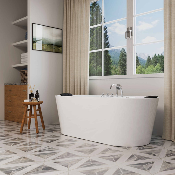 Modern white freestanding bathtub near large windows with forest view, wooden stool with toiletries, geometric tile floor, and soft curtains.