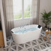 Modern white freestanding bathtub filled with water, placed on geometric tile floor near sheer-curtained window with green view, wooden stool and potted plant nearby.