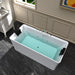 Modern white freestanding bathtub filled with blue-green water, sitting on dark tile floor with paneled wall and window in background.