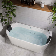 Modern white freestanding bathtub filled with blue water, surrounded by white subway tiles, hexagonal floor tiles, and green houseplants.