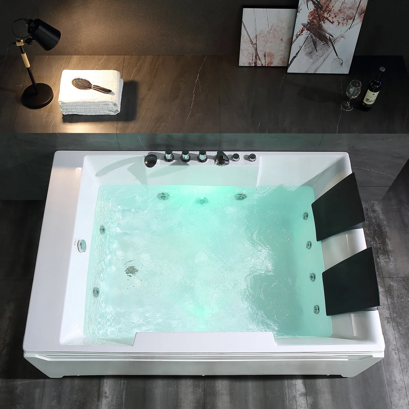 Large white jacuzzi tub filled with turquoise water, surrounded by dark tiled floor, with a desk lamp and folded towels nearby, and abstract art on the wall.