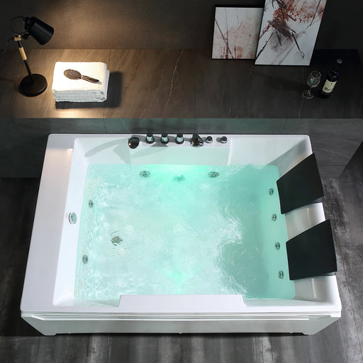 Large white jacuzzi tub filled with turquoise water, surrounded by dark tiled floor, with a desk lamp and folded towels nearby, and abstract art on the wall.
