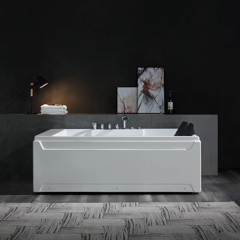 Modern white bathtub with chrome fixtures, positioned on textured floor against dark gray wall with art and lamp