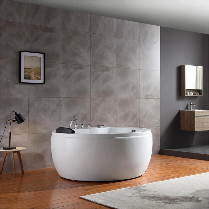 Modern bathroom with white freestanding tub, gray stone tiles, wooden floor, and minimalist decor including a table lamp and landscape artwork.