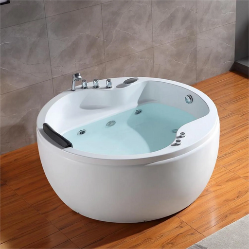 Modern round white jacuzzi tub with blue water, mounted on wooden floor with marble wall tiles and chrome fixtures.