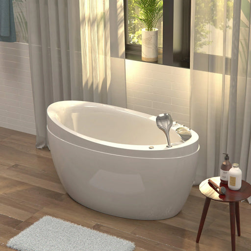 Modern white freestanding bathtub with silver faucet, next to sheer curtains and window with potted plant, small side table with bath products.