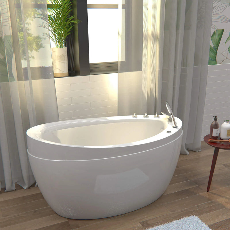 Modern white freestanding bathtub near soft curtains and window, with a green plant and bath products on a side table.