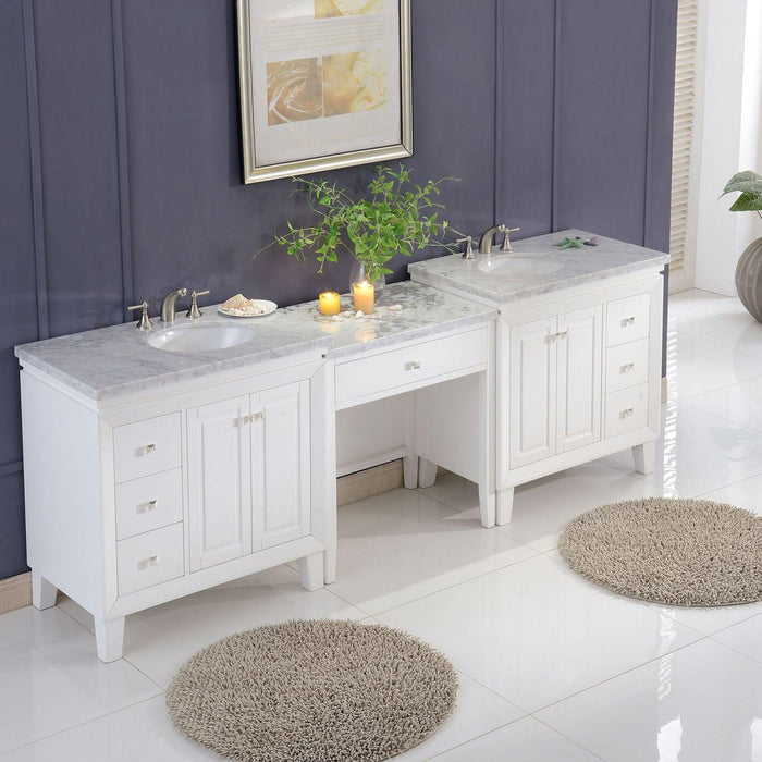 White bathroom vanity with marble top, two sinks, and central workspace, decorated with green plant, candles, and shaggy round rugs on glossy tile floor.
