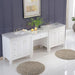 White bathroom vanity with marble top, two sinks, and central workspace, decorated with green plant, candles, and shaggy round rugs on glossy tile floor.