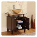 Dark wood bathroom vanity with stone vessel sink, open cabinet revealing rolled towels, and slender vases with pink branches.