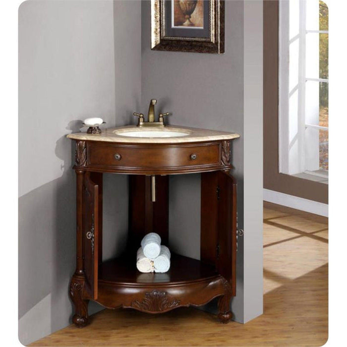 Ornate wooden corner bathroom vanity with marble top, brass faucet, and rolled white towels on lower shelf.