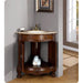 Ornate wooden corner bathroom vanity with marble top, brass faucet, and rolled white towels on lower shelf.