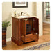 Wooden bathroom vanity with marble top, open cabinet revealing woven basket, ornate carved column, soap dispenser, and window in background.
