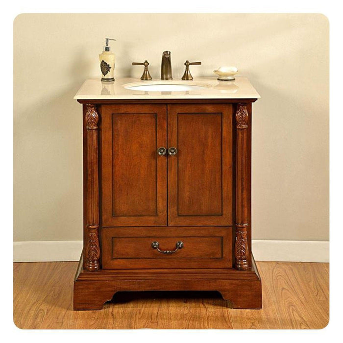 Traditional wooden bathroom vanity with marble top, decorative columns, and bronze fixtures and soap dispenser.