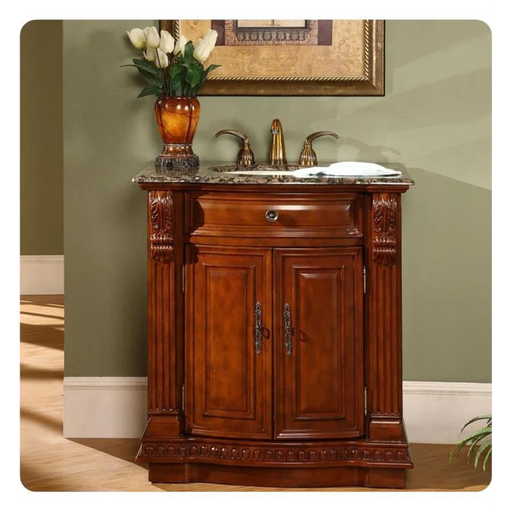 Traditional wooden bathroom vanity with marble top, decorative carved details, and bronze faucet, with white tulips in an amber vase.