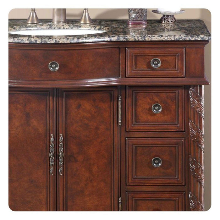 Rich mahogany bathroom vanity with ornate hardware, marble countertop, and decorative carved details on cabinet doors and drawers.