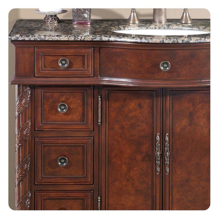 Rich mahogany bathroom vanity with ornate drawers, decorative hardware, and a speckled granite countertop with an undermount sink.