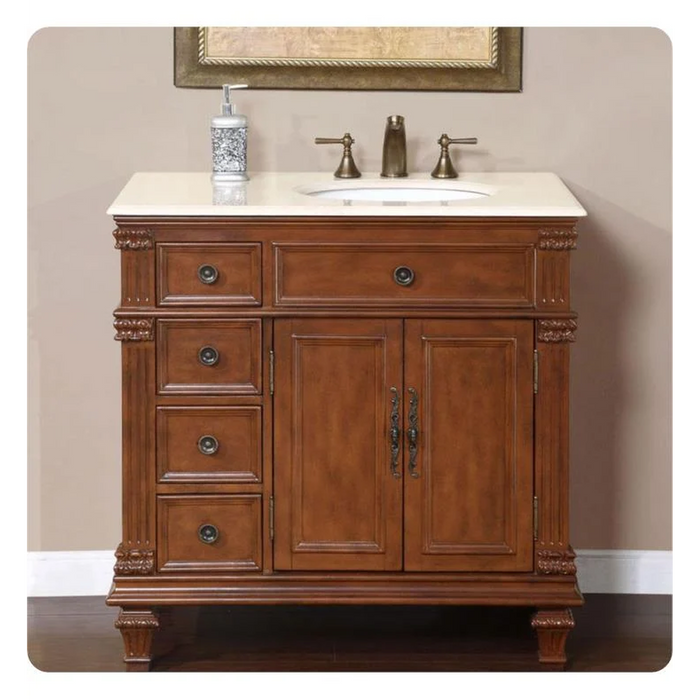 Ornate wooden bathroom vanity with four drawers, two cabinet doors, white marble top, and bronze faucet fixtures.