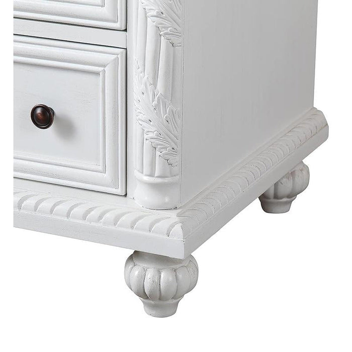 White wooden dresser corner with ornate carved details, dark round knob, and decorative bun foot
