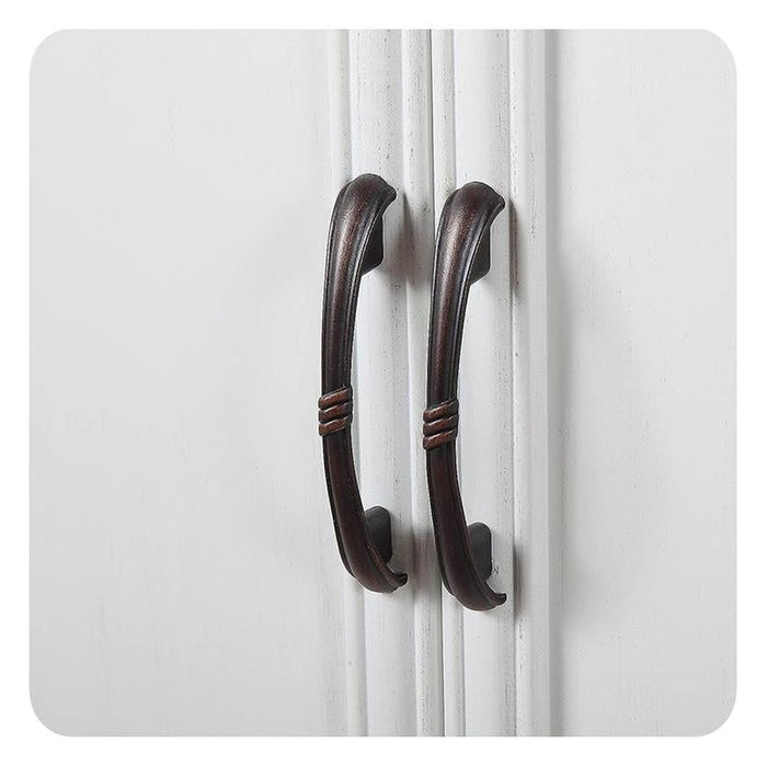 Two dark wooden curved door handles on a white paneled surface, with decorative twisted details at their center.