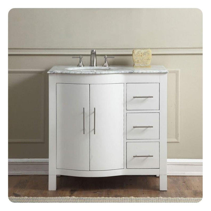 White bathroom vanity with marble countertop, curved cabinet doors, three drawers, and silver faucet against neutral wall.