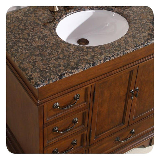 Wooden bathroom vanity with Baltic brown granite countertop and white ceramic undermount sink, featuring ornate metal drawer pulls.