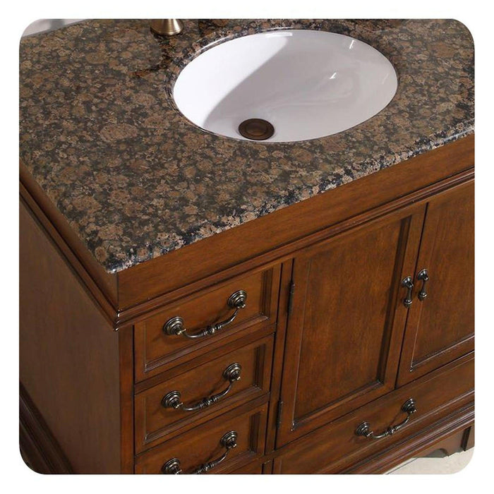 Wooden bathroom vanity with Baltic brown granite countertop and white ceramic undermount sink, featuring ornate metal drawer pulls.