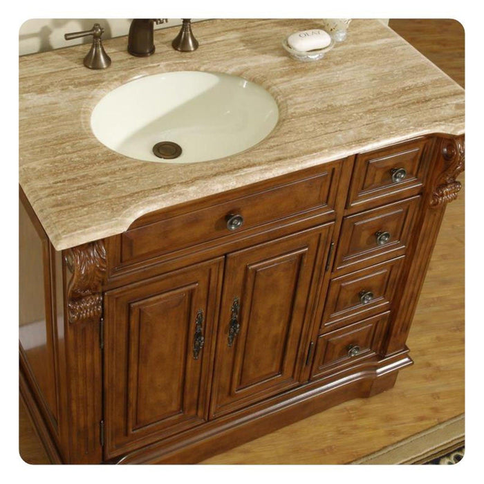Wooden bathroom vanity with travertine countertop, white sink, and ornate carved details on rich brown cabinetry