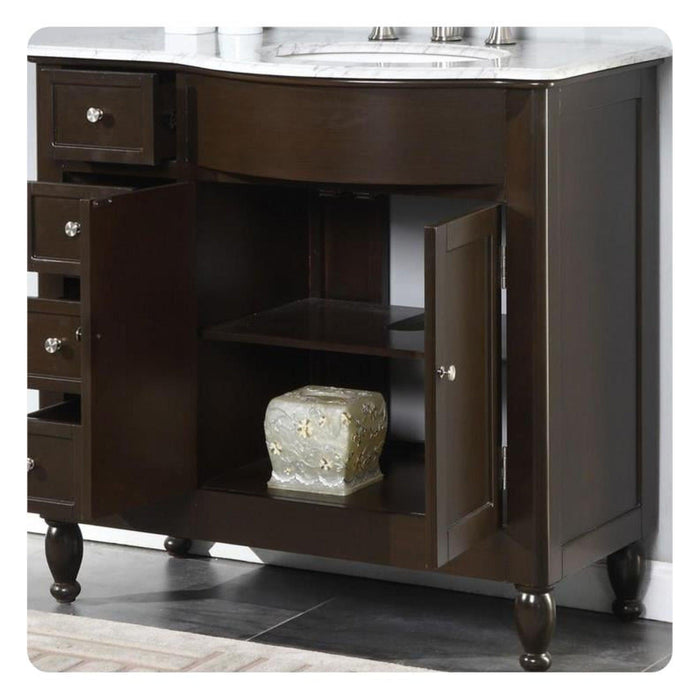 Dark wood bathroom vanity with marble top, three drawers, open shelf, and decorative turned legs, with ornate ceramic container on shelf.