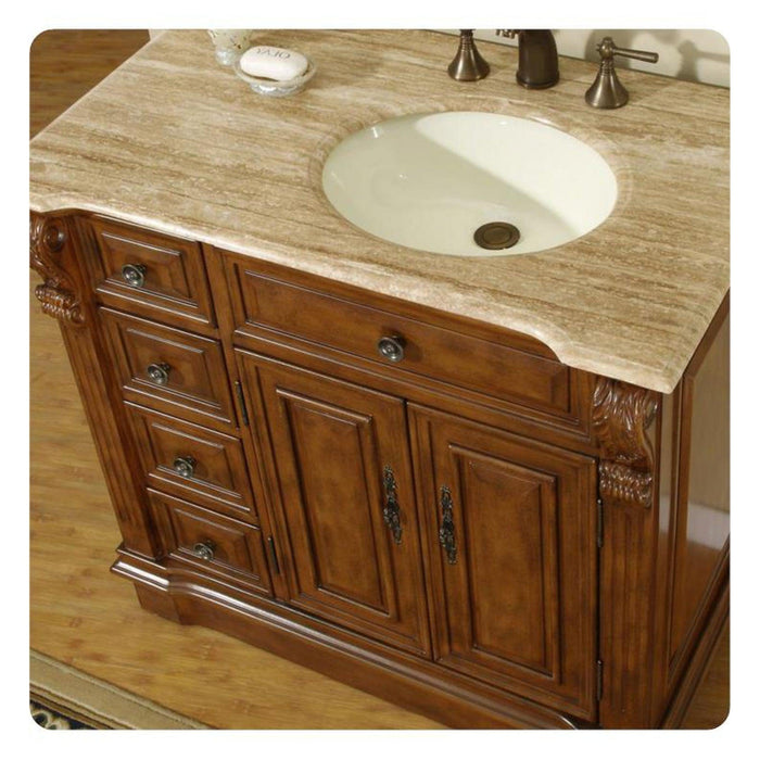 Antique-style wooden bathroom vanity with travertine countertop, white sink, and ornate carved details on cabinet
