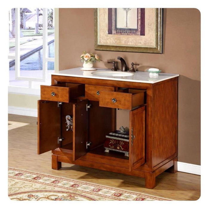 Wooden bathroom vanity with white marble top, open drawers, cabinet doors, and decorative floral arrangement near sink