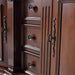 Ornate wooden cabinet with decorative drawer pulls and carved vertical lines, rich brown wood finish with intricate metal handles.