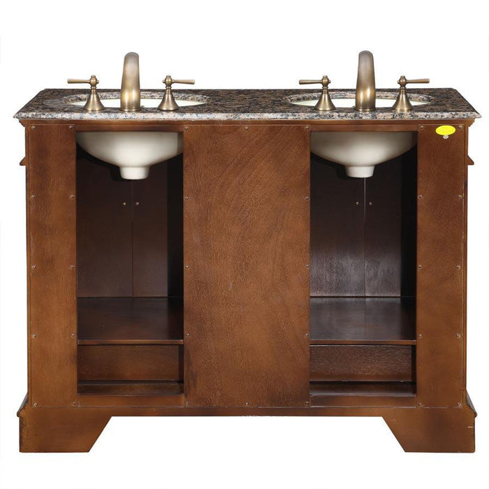 Wooden bathroom vanity with granite top, two white sinks, and brass faucets, featuring open storage compartments on sides.