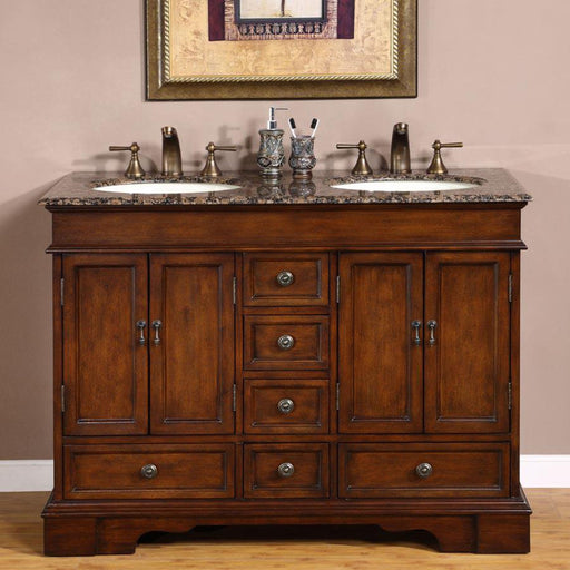 Elegant wooden bathroom vanity with dark brown finish, marble countertop, double sinks, bronze faucets, and decorative accessories against a pale pink wall.