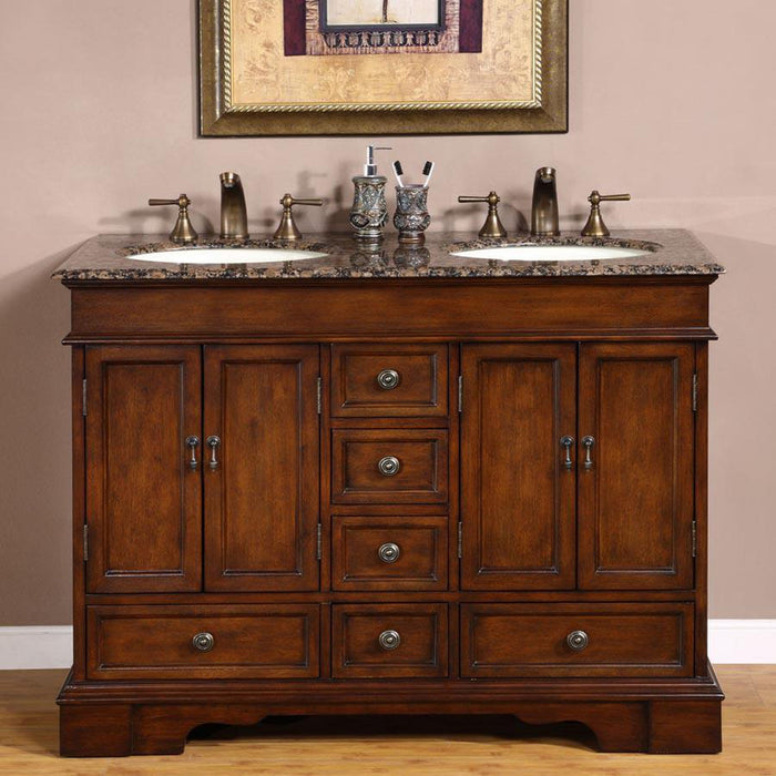 Elegant wooden bathroom vanity with dark brown finish, marble countertop, double sinks, bronze faucets, and decorative accessories against a pale pink wall.