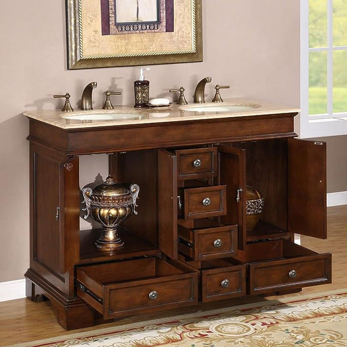 Dark wood bathroom vanity with marble top, multiple drawers, double sinks, and decorative bronze urn, framed by ornate mirror and window.
