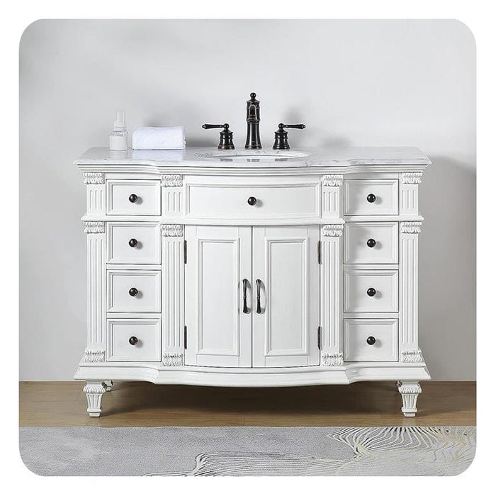 Elegant white bathroom vanity with six drawers, black fixtures, marble top, and ornate carved details on legs and columns.