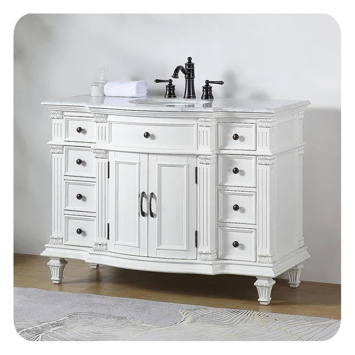 White ornate bathroom vanity with six drawers, marble top, and black fixtures, sitting on a textured rug.
