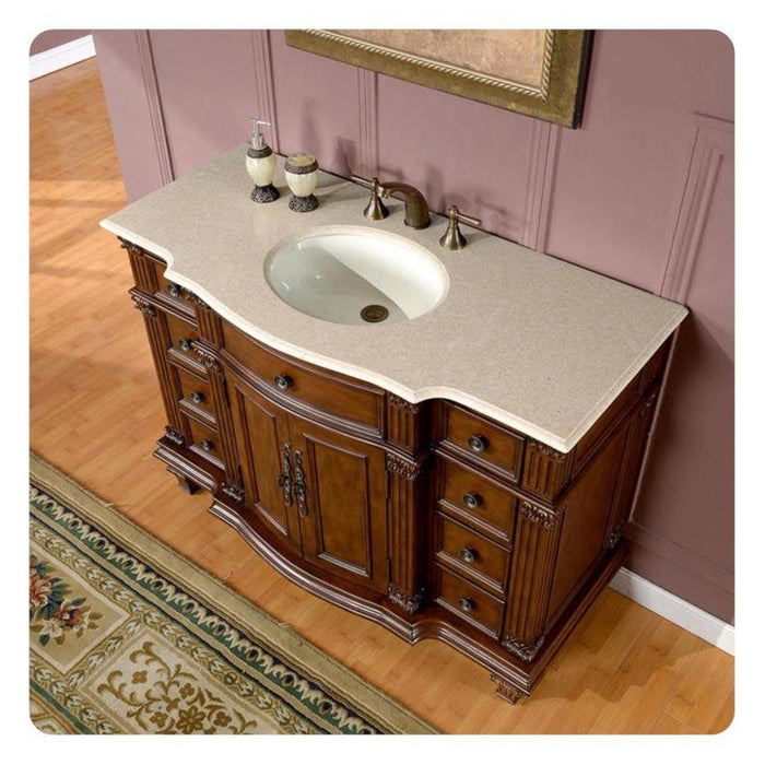 Ornate wooden bathroom vanity with curved design, white marble top, oval sink, and bronze fixtures on pink wall