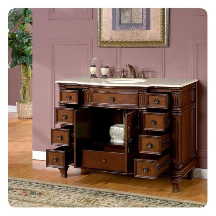 Antique wooden bathroom vanity with multiple drawers, marble top sink, decorative soap dispensers, and ornate details against pink wall.