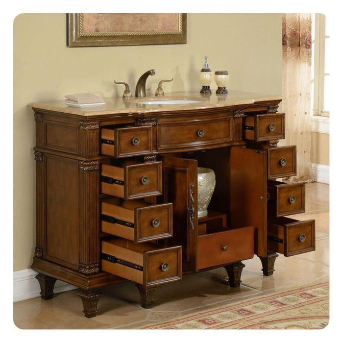 Antique wooden bathroom vanity with multiple open drawers, marble top sink, and decorative hardware, placed on an ornate area rug.
