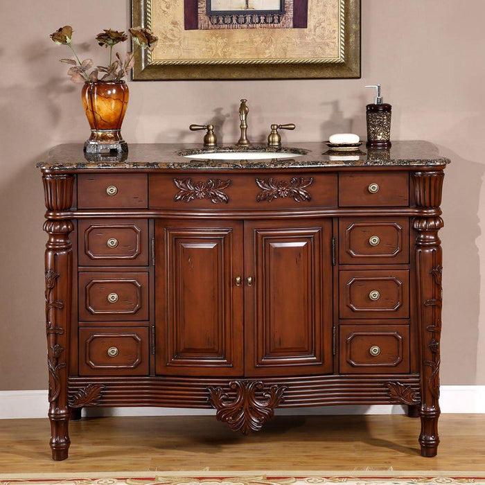 Elegant wooden bathroom vanity with carved details, granite top, undermount sink, and decorative amber vase with dried flowers.