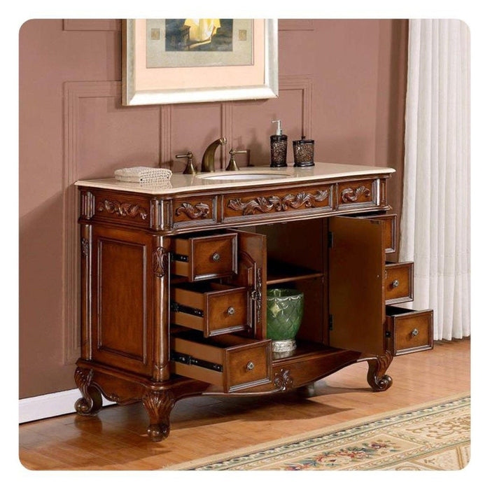 Ornate wooden bathroom vanity with carved details, marble top, open drawers, and sink with bronze fixtures.