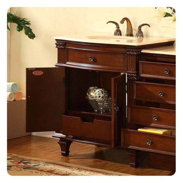 Elegant wooden bathroom vanity with marble top, ornate bronze faucets, and decorative carved details, with rolled towels and a patterned rug visible.