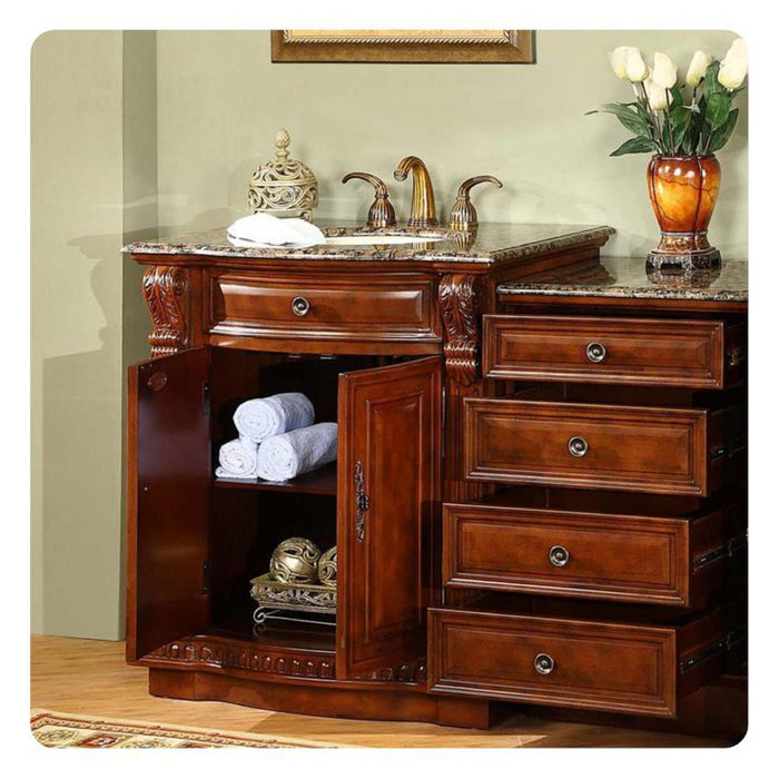 Rich wood bathroom vanity with marble top, open cabinet with white towels, decorative vase with white tulips, and ornate gold faucet.