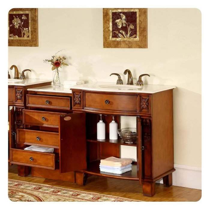 Rich wood bathroom vanity with double sinks, ornate drawers, floral artwork, and folded towels on open shelving.
