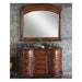 Ornate wooden bathroom vanity with curved design, double sinks, granite top, and matching arched mirror on stone wall with small plant.